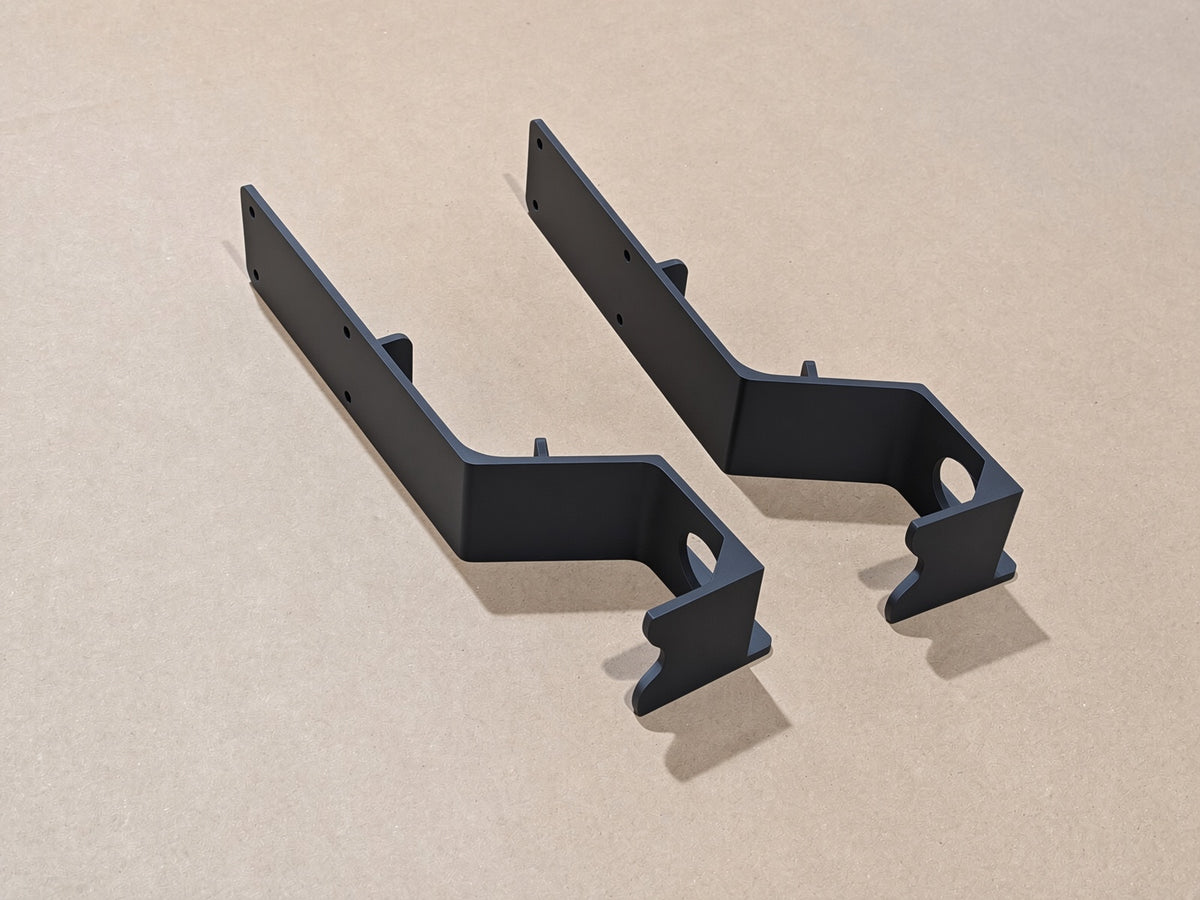 Two matte black elddis tap brackets with pre-drilled screw holes, displayed on a light beige textured background.